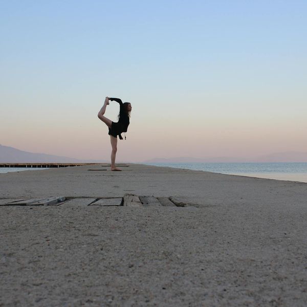 Person balancing on one leg in a yoga posture outdoors at sunset.