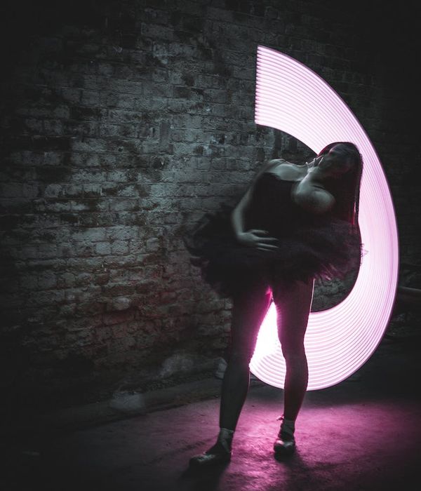 Woman performing a graceful yoga pose in a dark room with pink light.